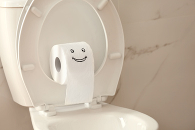 Photo of Roll of paper with funny face on toilet bowl in bathroom