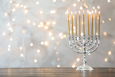 Photo of Hanukkah menorah with candles on table against blurred lights