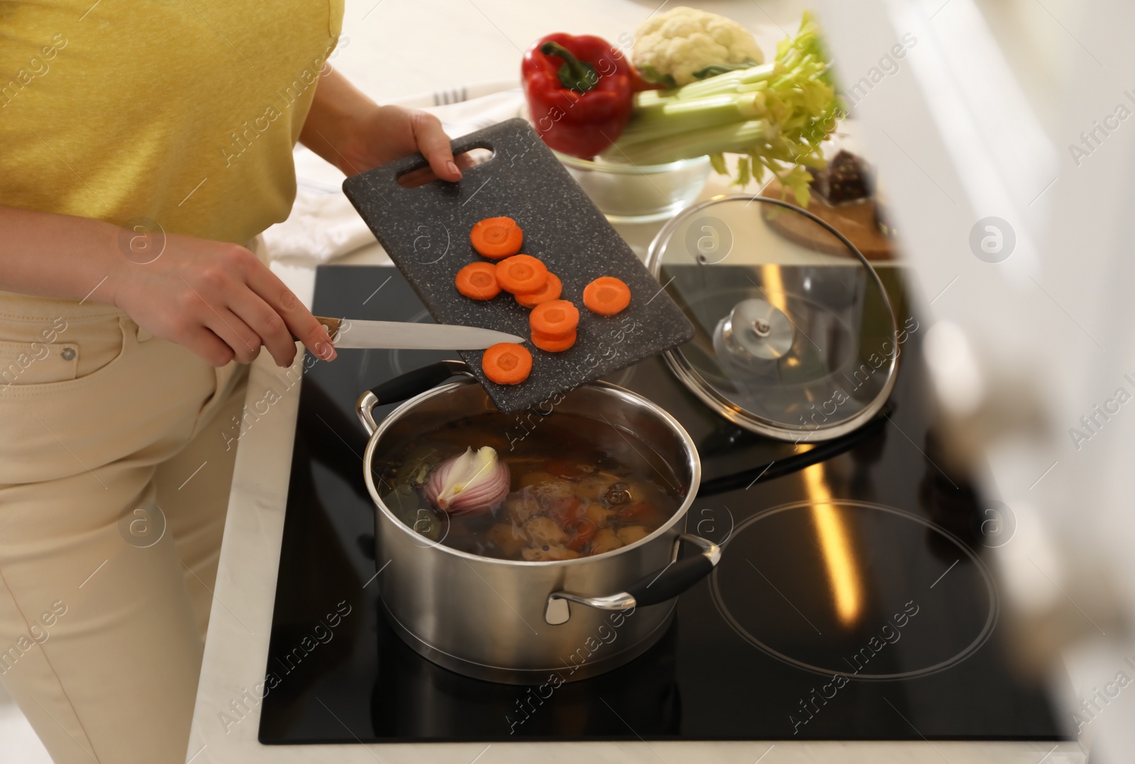 Photo of Woman putting carrot into pot to make bouillon in kitchen, closeup. Homemade recipe