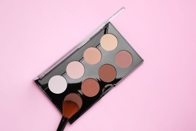 Photo of Colorful contouring palette and brush on pink background, top view. Professional cosmetic product