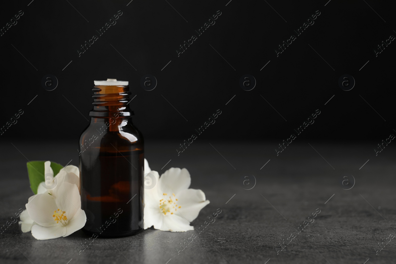 Photo of Essential oil and jasmine flowers on grey table. Space for text