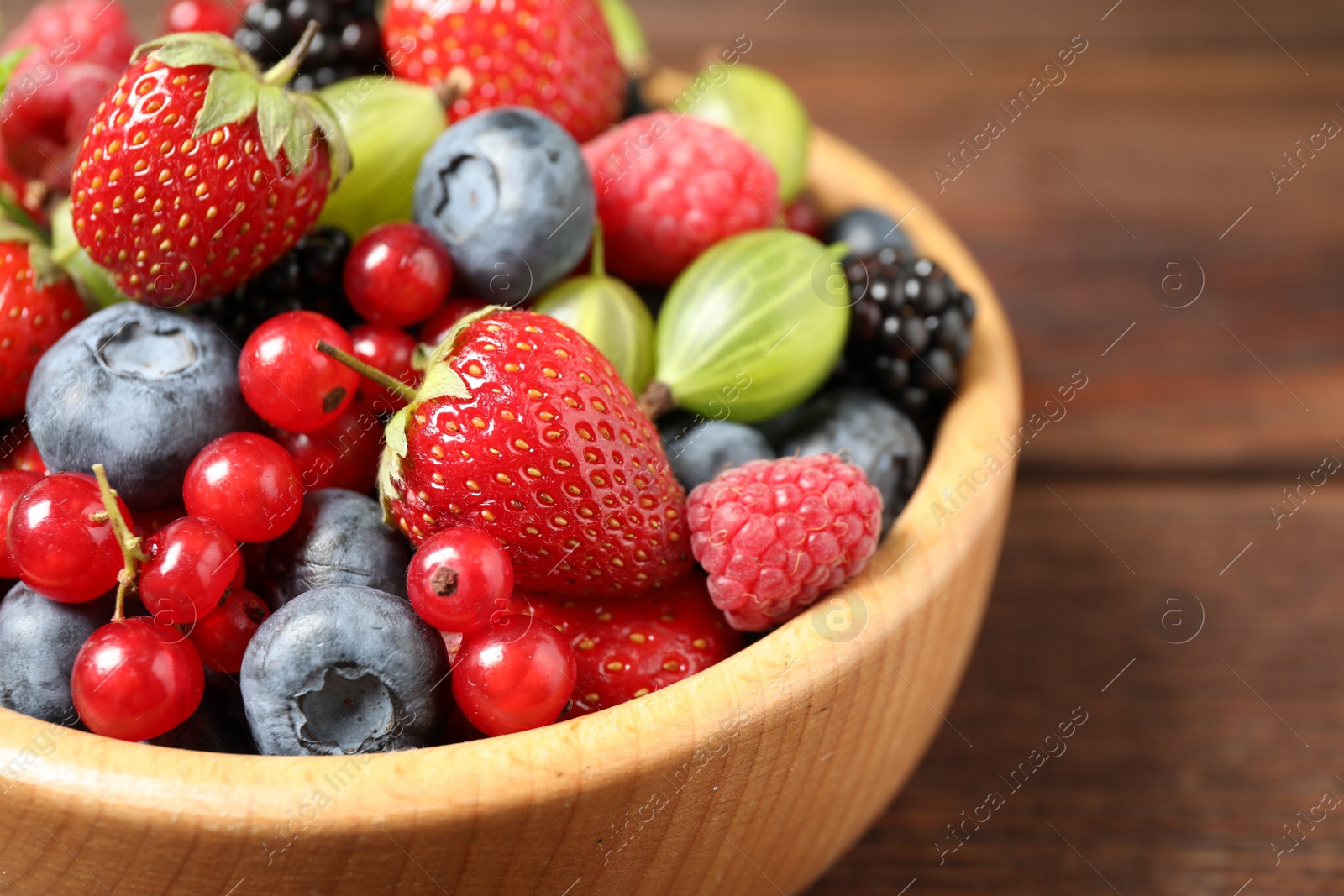 Photo of Mix of ripe berries in wooden bowl on table, closeup