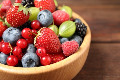 Mix of ripe berries in wooden bowl on table, closeup