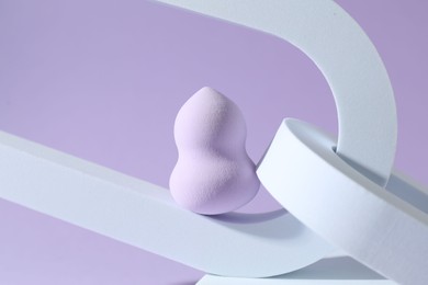 Stylish presentation of makeup sponge on violet background