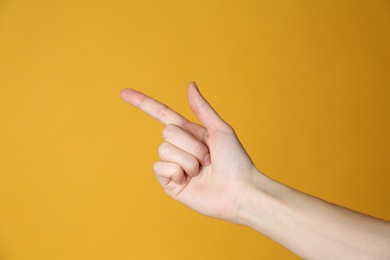 Photo of Woman pointing at something on yellow background, closeup. Finger gesture