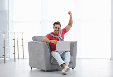 Photo of Handsome young man with laptop in armchair indoors. Space for text