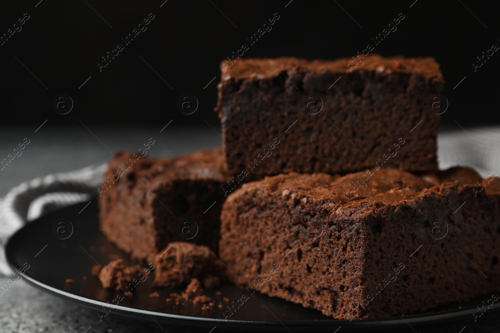 Photo of Plate with fresh brownies on grey table against black background, space for text. Delicious chocolate pie