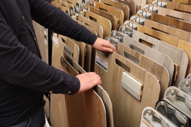 Photo of Man choosing wooden flooring among different samples in shop, closeup