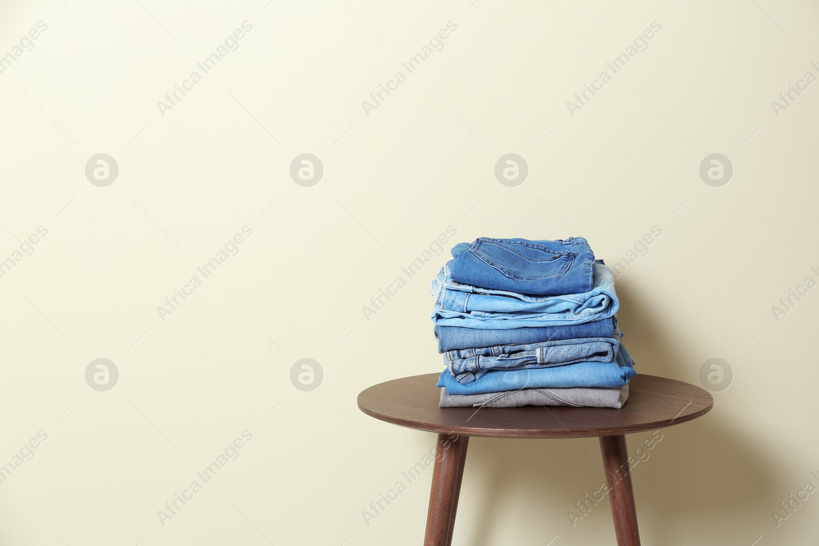 Photo of Stack of different jeans on table against light background. Space for text