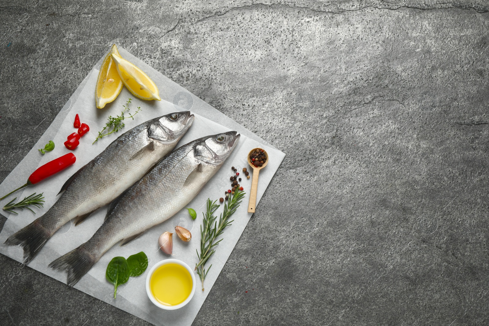 Photo of Sea bass fish and ingredients on grey table, top view. Space for text