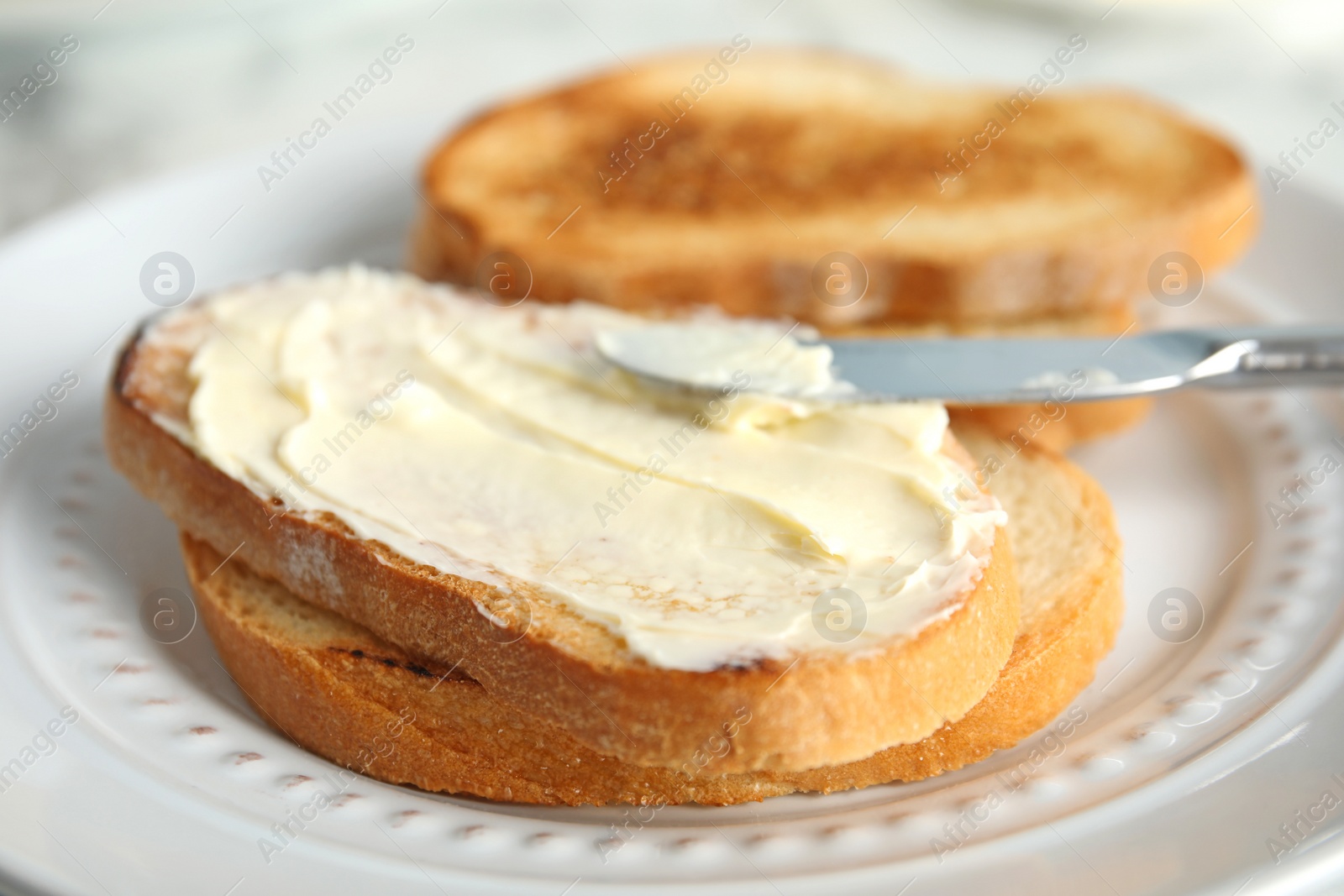 Photo of Tasty bread with butter and knife on plate, closeup