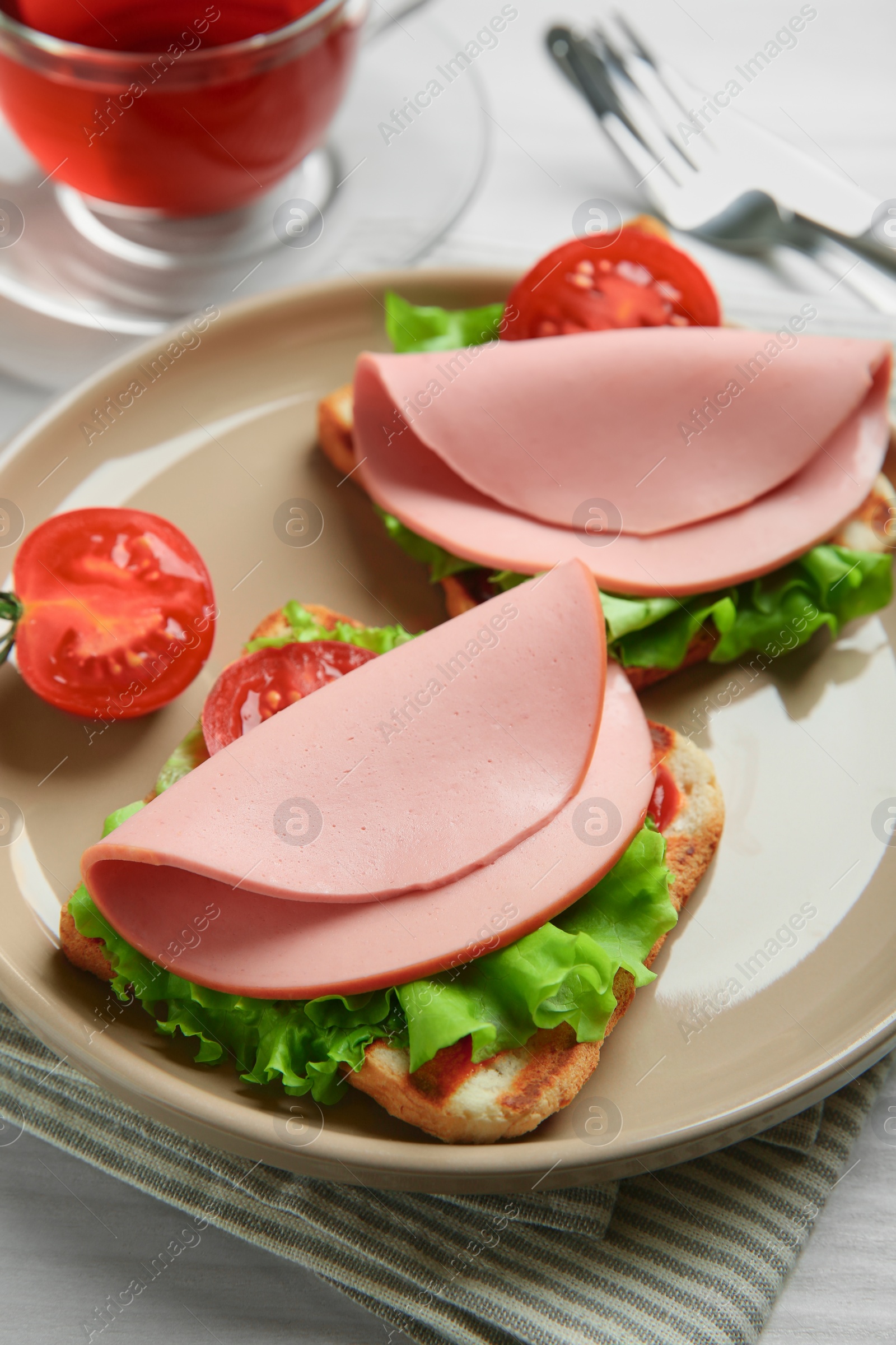 Photo of Plate of tasty sandwiches with boiled sausage, tomato and lettuce on white wooden table, closeup