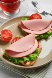 Plate of tasty sandwiches with boiled sausage, tomato and lettuce on white wooden table, closeup