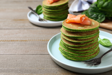 Tasty spinach pancakes with salmon on wooden table, closeup. Space for text