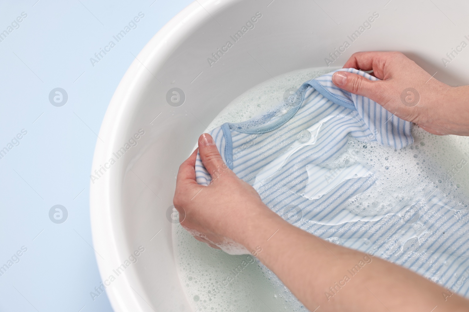 Photo of Woman washing baby clothes in basin on light blue background, top view