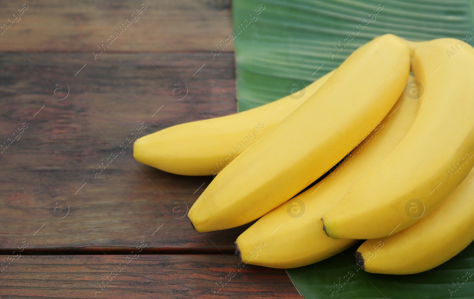 Photo of Delicious bananas and green leaf on wooden table. Space for text