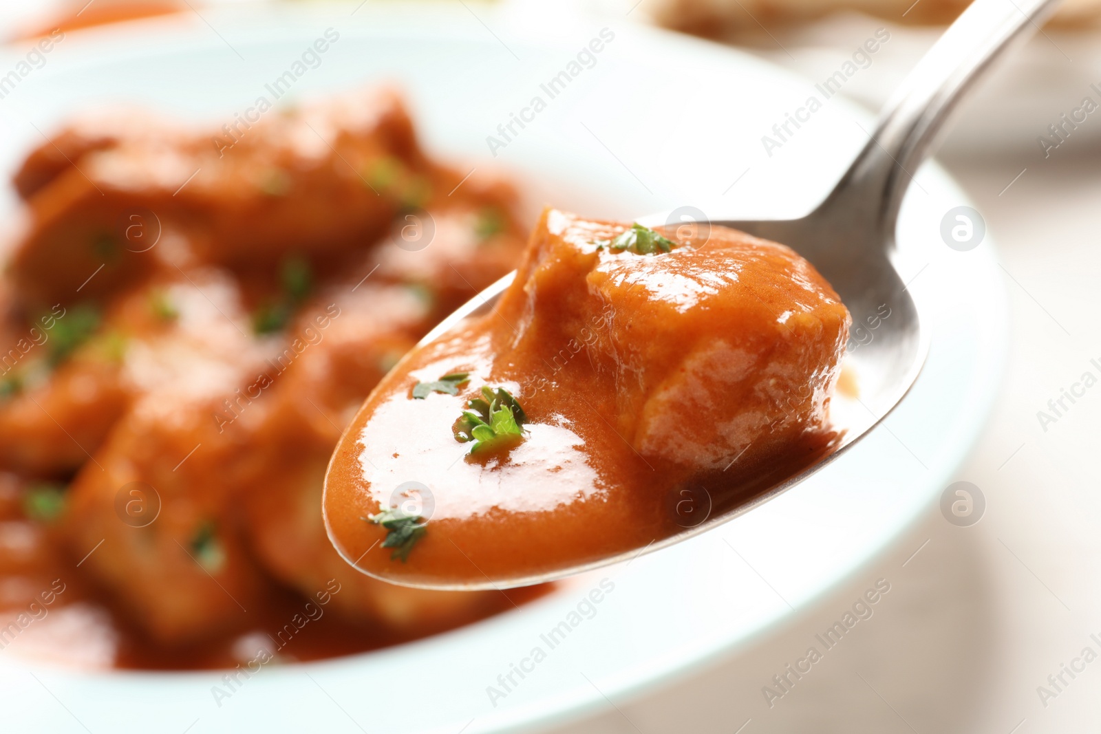 Photo of Tasty butter chicken in spoon over plate with meal. Traditional Murgh Makhani dish