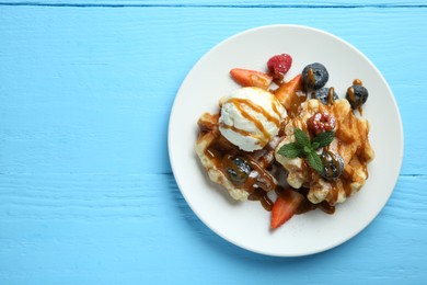 Photo of Delicious Belgian waffles with ice cream, berries and caramel sauce on light blue wooden table, top view. Space for text