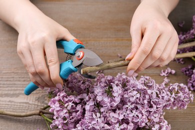 Woman trimming lilac branches with secateurs at wooden table, closeup
