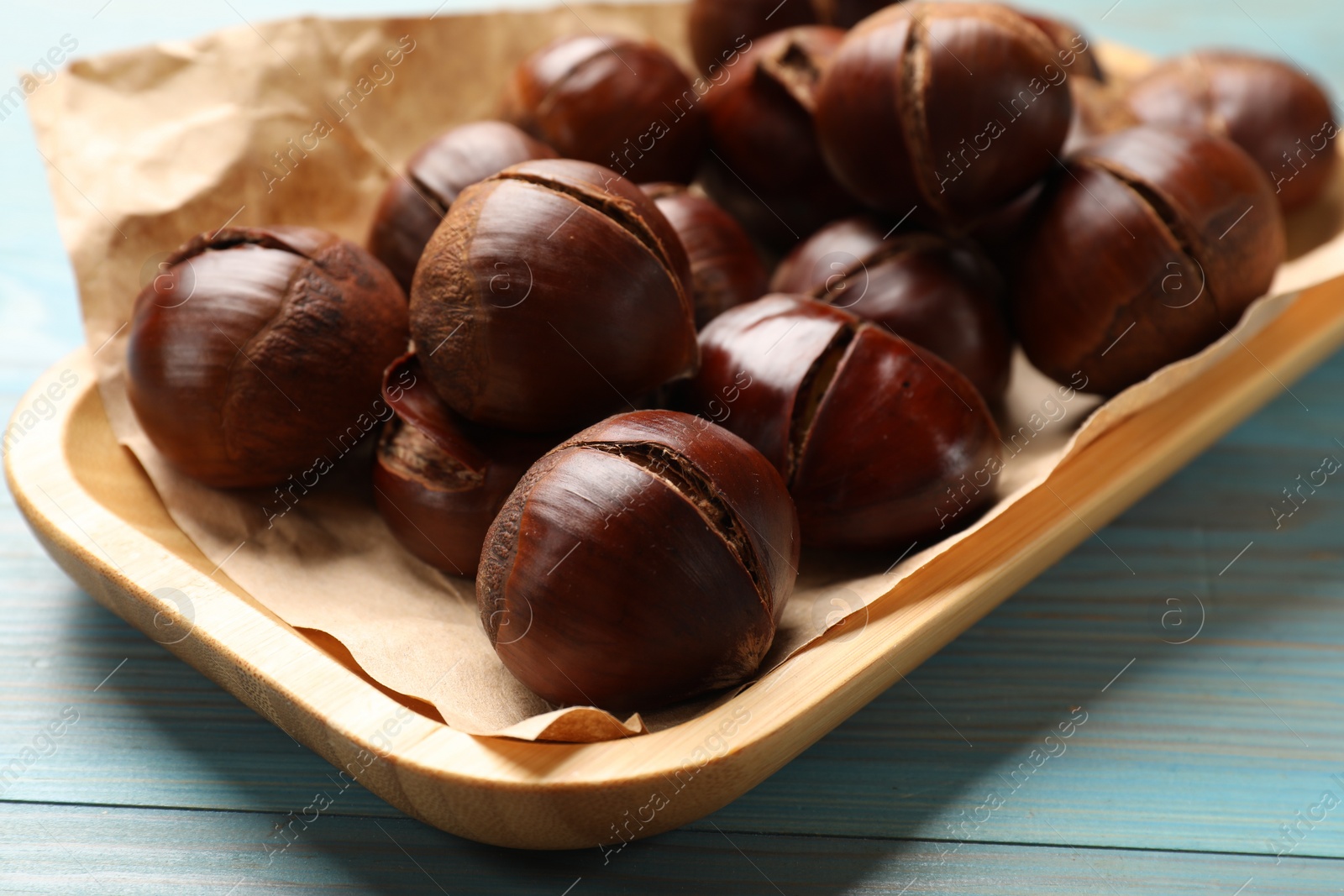 Photo of Fresh edible sweet chestnuts in serving plate on light blue wooden table, closeup