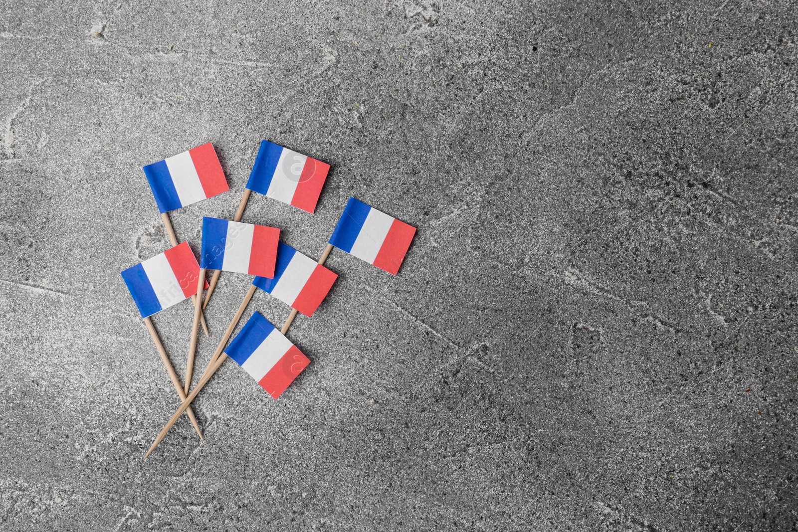 Photo of Small paper flags of France on grey table, flat lay. Space for text