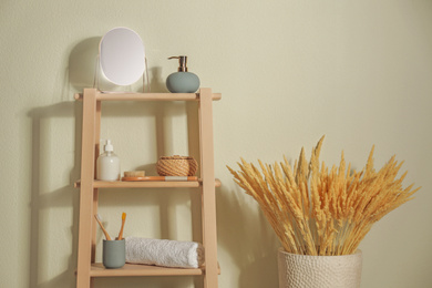 Wooden shelving unit with toiletries near light wall indoors. Bathroom interior element