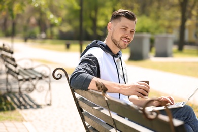 Photo of Portrait of young man with laptop and cup of coffee on bench in park