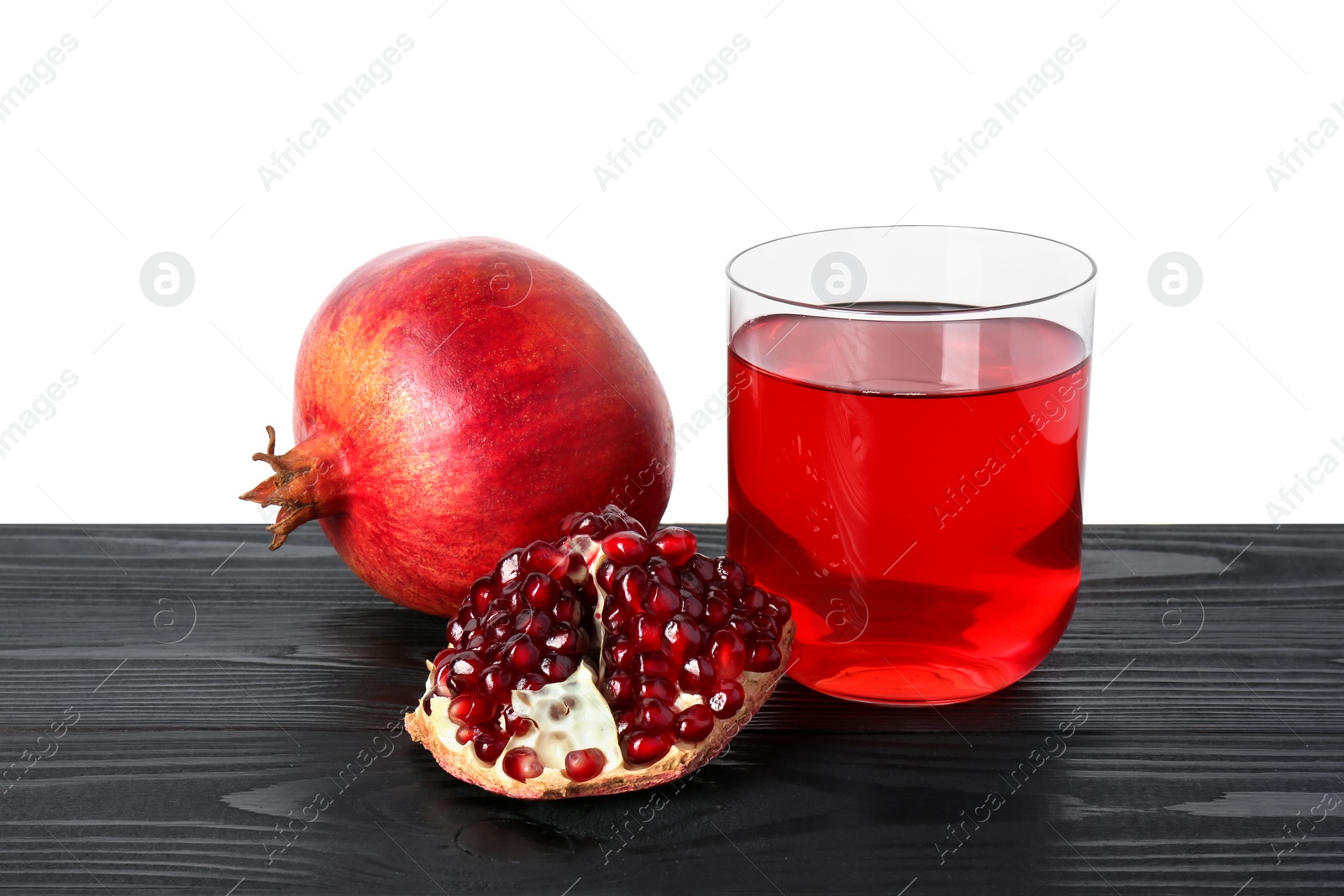 Photo of Refreshing pomegranate juice in glass and fruits on black wooden table against white background