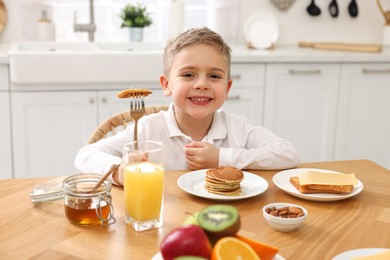 Photo of Cute little boy having breakfast at table in kitchen