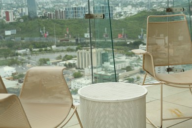 Coffee table and beige chairs against picturesque landscape of city in cafe