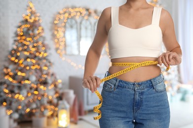 Image of Woman measuring waist with tape in room decorated for Christmas, closeup