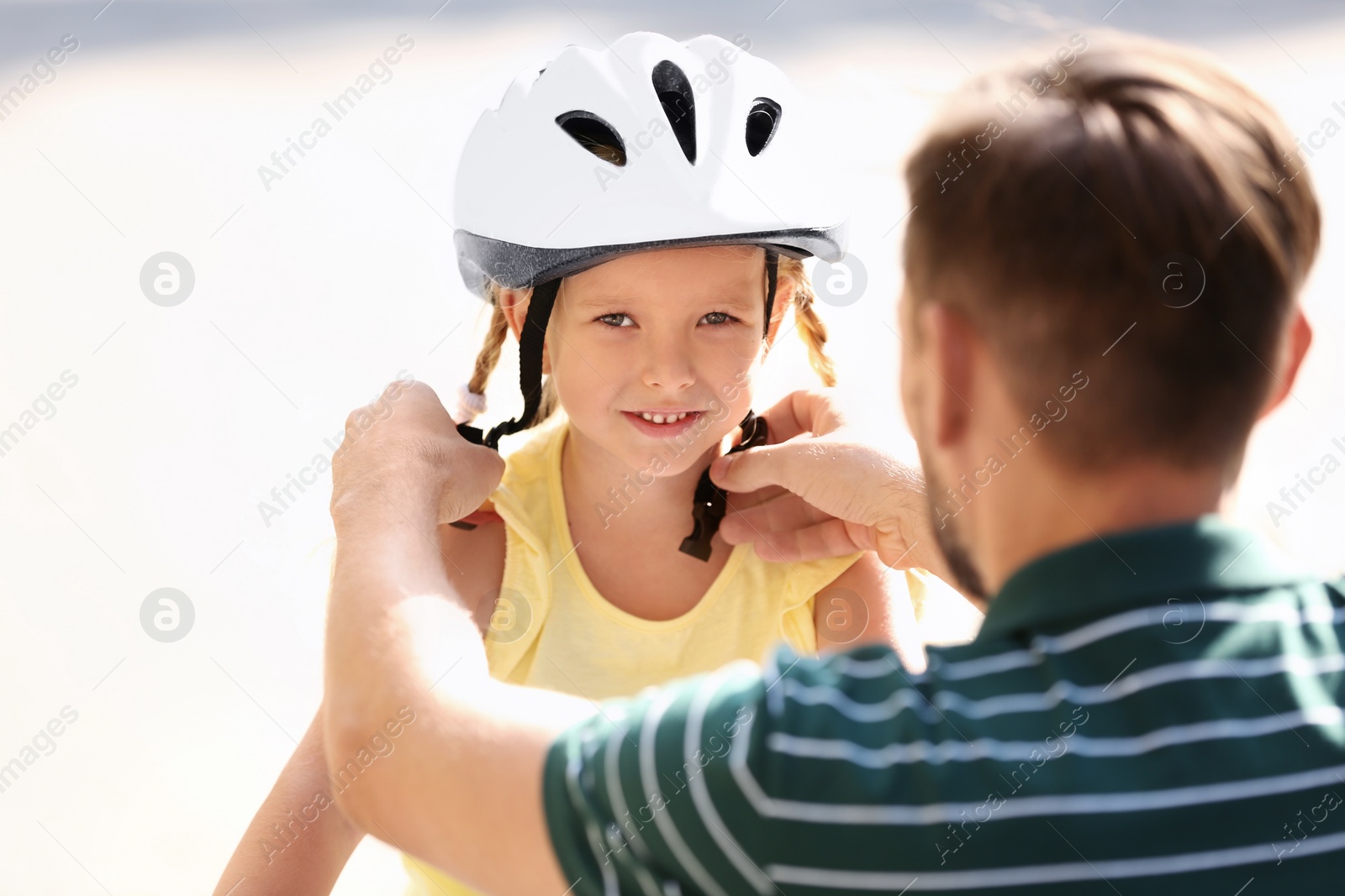 Photo of Father putting on bicycle helmet on his daughter outdoors