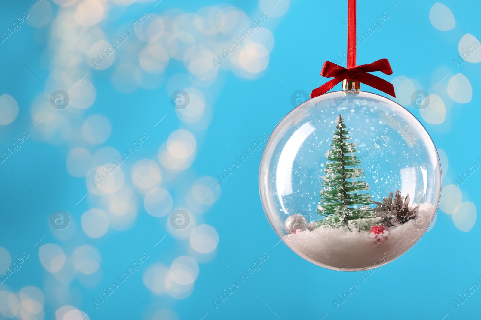 Photo of Decorative snow globe hanging on against blurred festive lights, closeup. Space for text