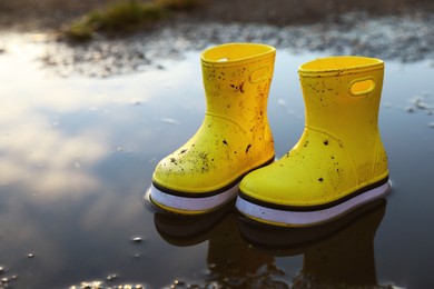 Photo of Yellow rubber boots in puddle outdoors, space for text. Autumn walk