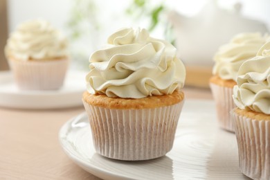 Photo of Tasty cupcakes with vanilla cream on light wooden table, closeup