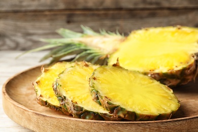 Photo of Cut fresh juicy pineapple on wooden tray, closeup