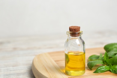 Photo of Wooden board with glass bottle of basil oil, leaves and space for text
