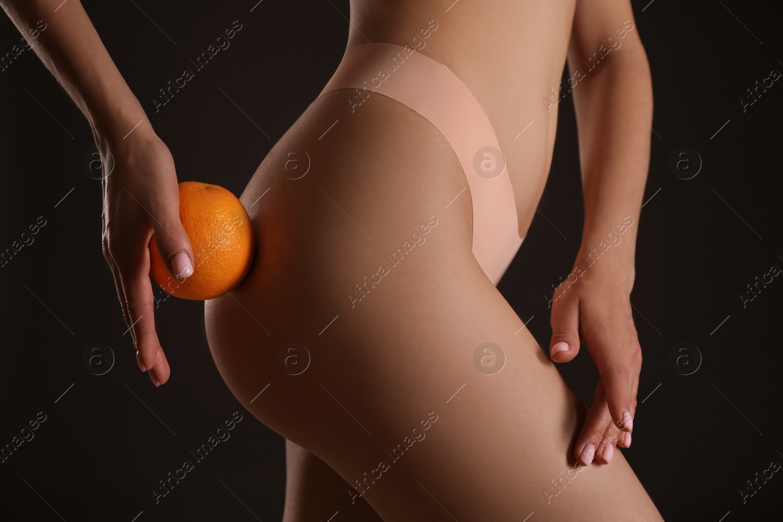 Photo of Closeup view of slim woman in underwear with orange on black background. Cellulite problem concept