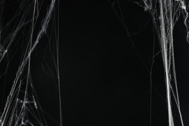 Photo of Creepy white cobweb on black background, space for text