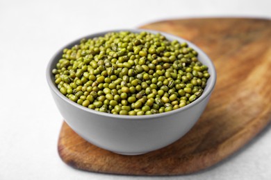 Photo of Bowl with green mung beans and wooden board on white table, closeup