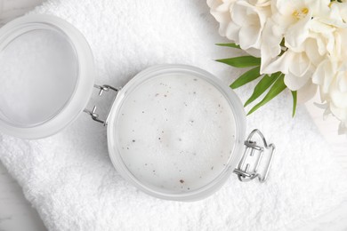 Photo of Jar of natural exfoliating salt scrub, white towel and freesia flowers on table, flat lay
