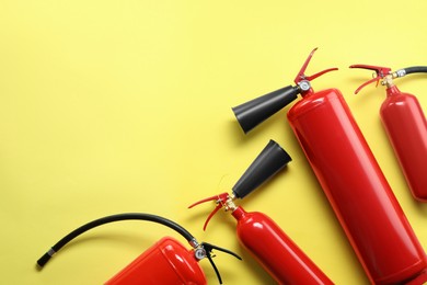 Photo of Many fire extinguishers on yellow background, flat lay. Space for text