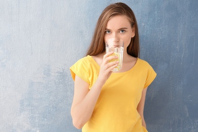 Young woman drinking lemon water on color background