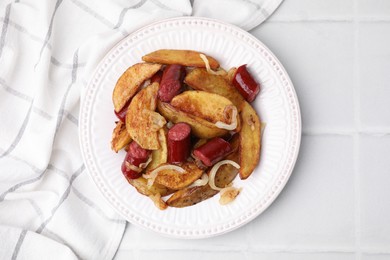 Photo of Delicious baked potato with thin dry smoked sausages and onion on white tiled table, top view