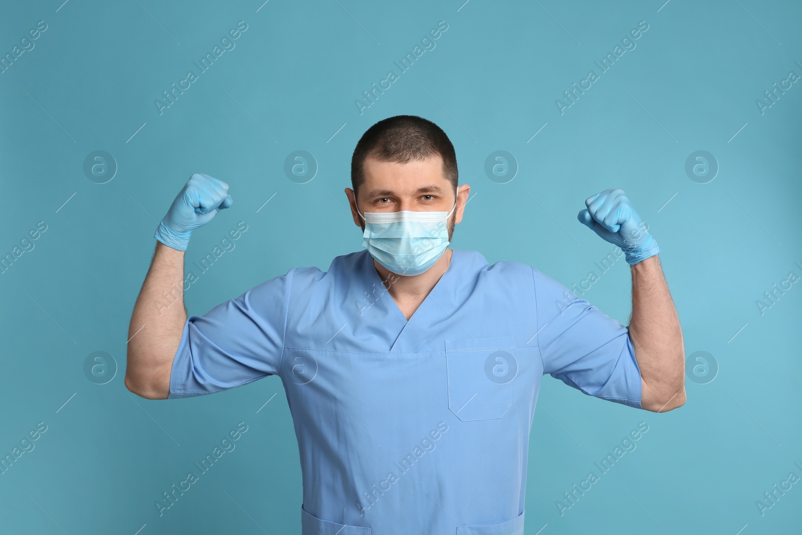 Photo of Doctor with protective mask showing muscles on light blue background. Strong immunity concept