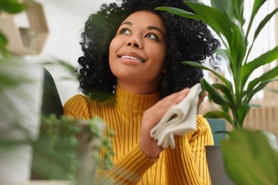 Photo of Happy woman wiping leafbeautiful potted houseplant indoors
