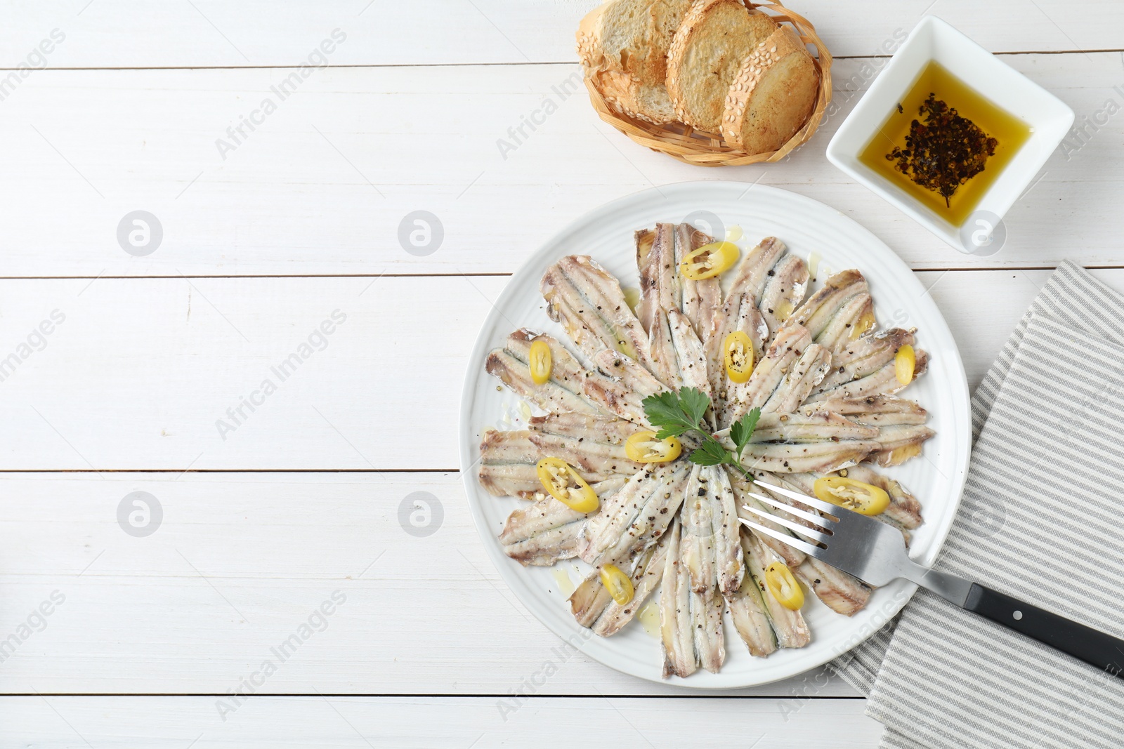 Photo of Tasty pickled anchovies served on white wooden table, flat lay. Space for text