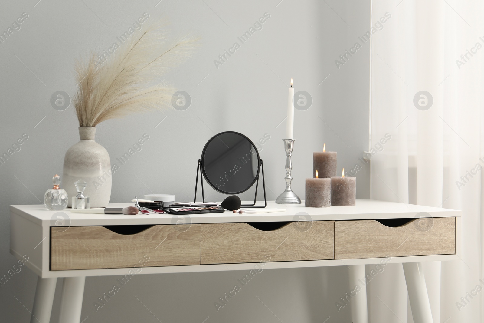 Photo of Dressing table with mirror, cosmetic products, perfumes and burning candles in makeup room