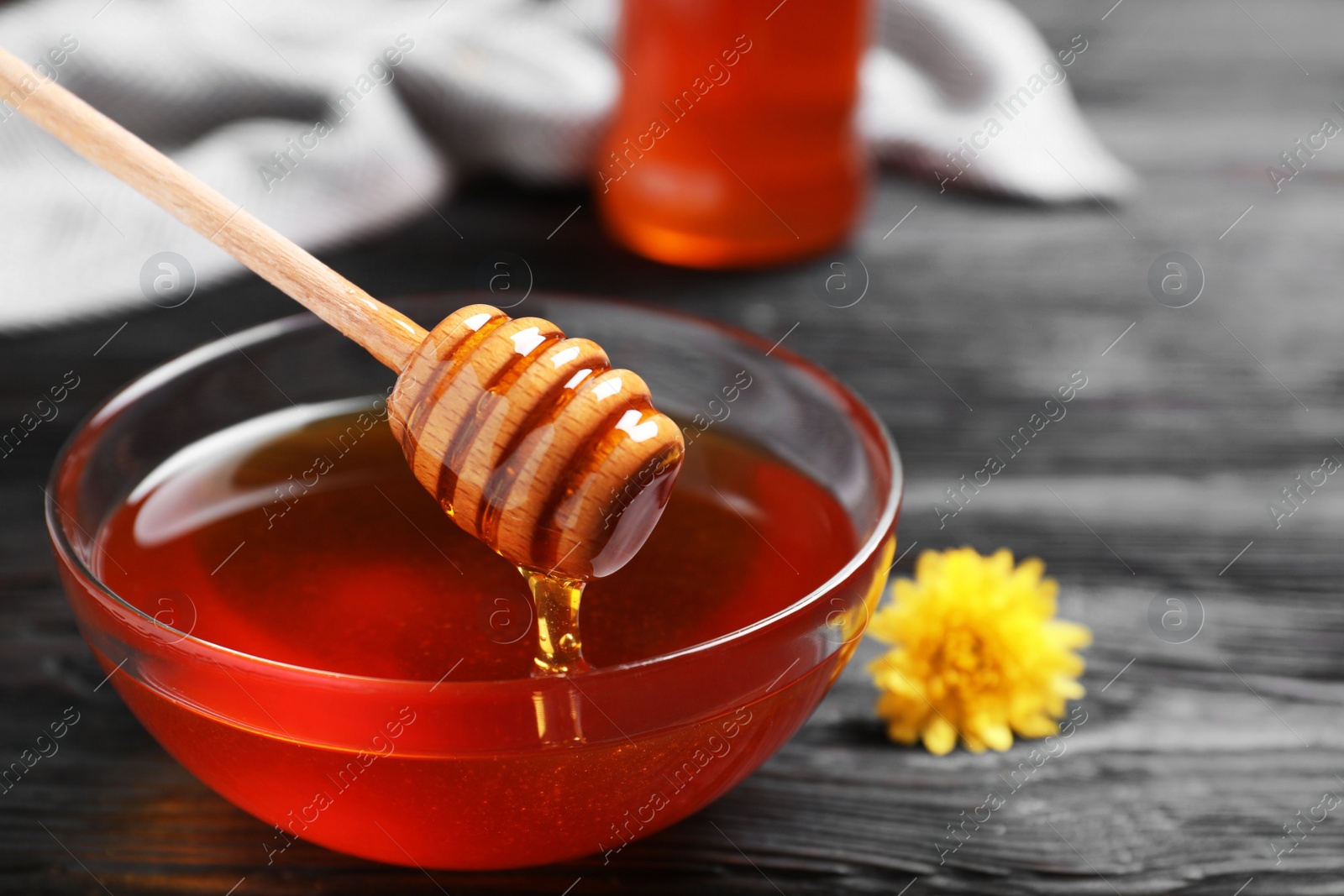 Photo of Glass bowl with organic honey and dipper on black wooden table, closeup