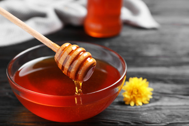 Glass bowl with organic honey and dipper on black wooden table, closeup